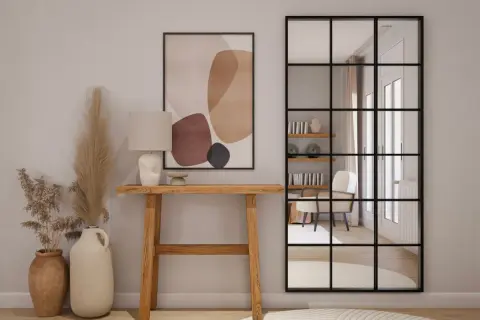 Entradas pequeñas con encanto: consola de madera, lámpara, cuadro abstracto y espejo industrial que refleja un sillón.