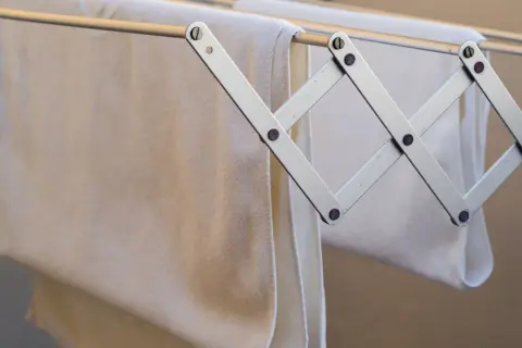Tendedero metálico con toallas blancas colgadas, ideal para colocar tendedero en fachada de SATE.