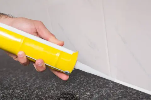 Mano aplicando silicona en juntas con pistola.