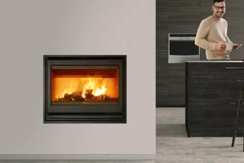 Chimenea cassette con fuego encendido. Un hombre sonríe con una taza y una tablet en una cocina moderna.