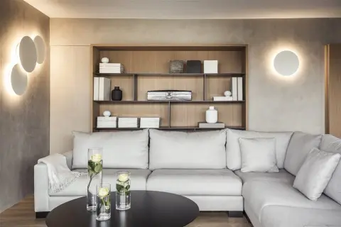 Iluminar un salón moderno con luces de pared circulares y una estantería de madera con objetos decorativos. Sofá gris y mesa negra con jarrones de rosas.
