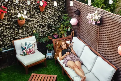Mujer relajada en un sofá en un patio con césped artificial, luces y plantas. Ideas para decorar patio sin dinero.