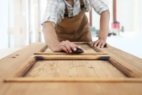 Carpintero lijando una puerta de sapelly para modernizarla.