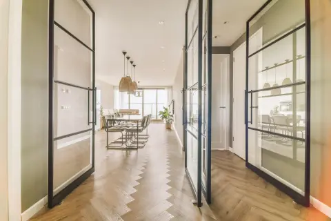 Amplio salón comedor rectangular de 25 metros, con suelo de espiga y separadores de cristal.