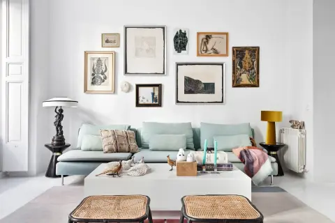 Un sofá azul claro con cojines decorativos y una colección de arte ecléctica en la pared. Ideas de qué poner detrás del sofá: una galería de arte o una estantería.