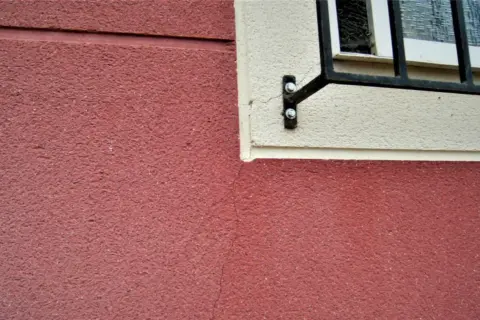 Detalle de juntas de dilatación en fachadas de color rojo y crema, con una ventana enrejada.