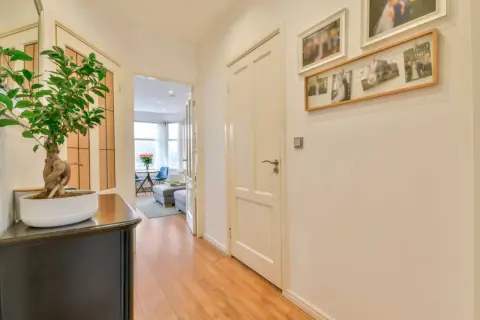 Un pasillo moderno y estrecho con suelo de madera, un bonsái y fotos familiares en la pared.