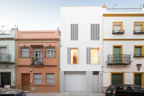 Fachada edificio con ladrillo visto y detalles de azulejos, junto a una moderna construcción blanca y otra amarilla con balcones de forja.