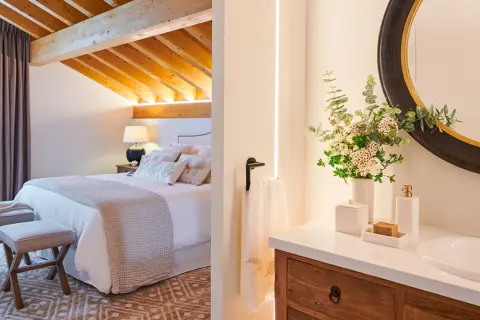 Habitación con vigas de madera y baño con espejo redondo. ¿Cuanto mide una habitación normal? Esta parece espaciosa.