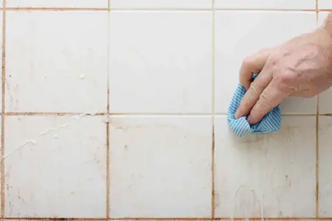 Mano limpiando juntas de azulejos sucias con un paño azul.