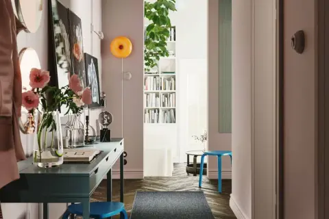 Un recibidor con pasillos con encanto: un escritorio azul, flores rosas, libros y un taburete.
