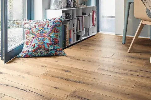 Suelo laminado de madera con un cojín colorido y estantería. Ideal para aprender como poner suelo laminado.