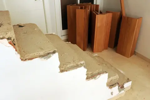 Preparativos para revestir escalera antigua. Tablas de madera apiladas junto a escalones de hormigón en proceso de reforma.