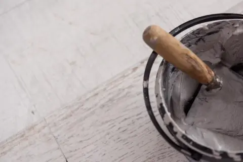 Paleta con morteros de revestimiento listos para aplicar sobre suelo de madera.