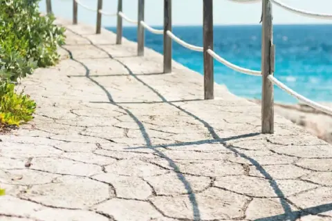 Camino de piedra con barandilla y mar azul. Un ejemplo de cómo hacer hormigón impreso para exteriores.
