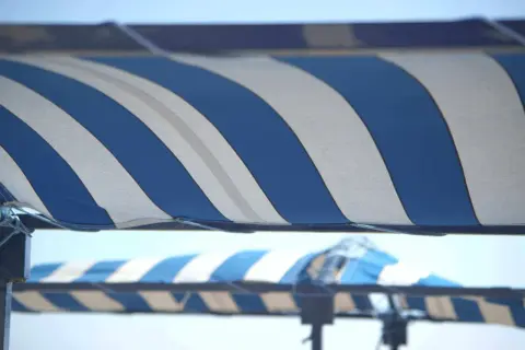 Toldo a rayas azules y blancas, listo para cambiar la tela y proteger del sol.