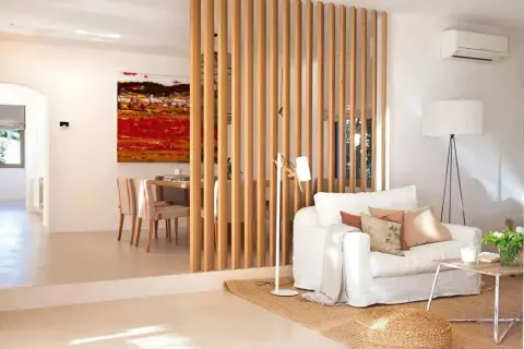 Elegante separador de madera para dividir salón en dos ambientes. Sofá blanco, mesa de centro rústica y cuadro vibrante.