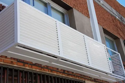 Carcasa blanca con lamas horizontales protege un aire acondicionado en fachada exterior.