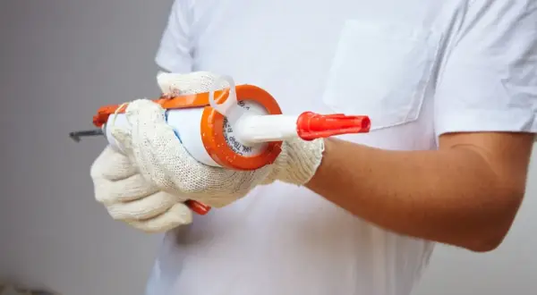 Manos enguantadas sujetan pistola de silicona, preparándose para sellar. ¿Cuánto tarda en secar la silicona?