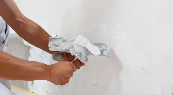 Man aplicando revoco en una pared con una llana. El revoco es un material de construcción para alisar y proteger superficies.