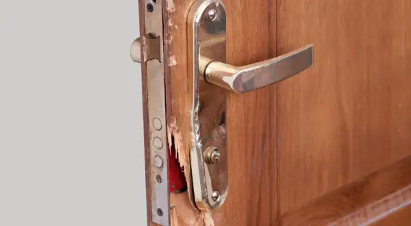 Puerta de contrachapado dañada, lista para reparar. Se ve el mecanismo de la cerradura y la manilla dorada.