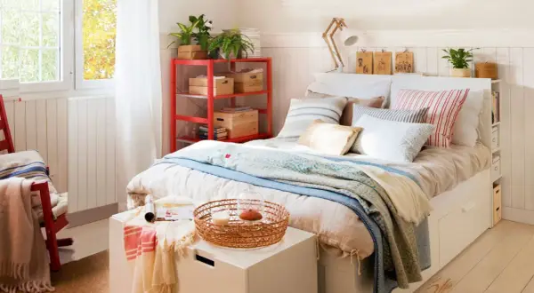 Acogedora habitación pequeña para adultos con cama, estantería roja y ventana luminosa.