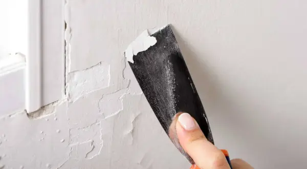 Raspando pintura descascarada de una pared. Un buen truco para pintar paredes es preparar la superficie.
