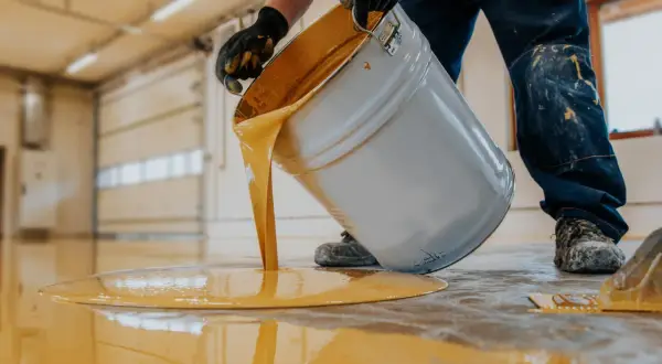Hombre con guantes vierte pintura amarilla de un cubo para pintar suelo cocina.