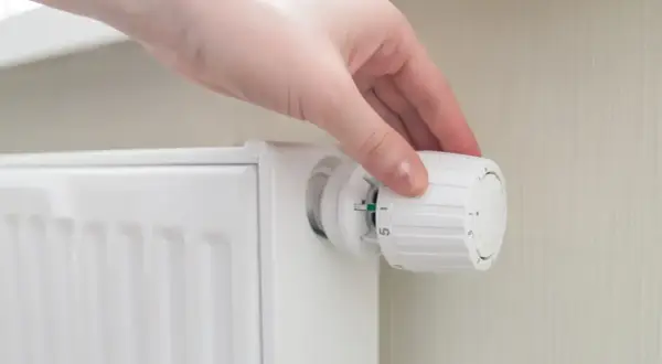 Mano ajustando el termostato para poner calefacción en casa. El radiador blanco está listo para calentar.