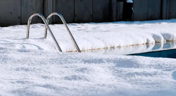 Escaleras de piscina asoman entre la nieve. Un reto para mantener piscina en invierno sin tapar.