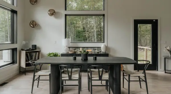 Mesa de comedor moderna con sillas de madera y asientos de mimbre. Un jarrón blanco y dos candelabros negros decoran la mesa, perfecta para decorar mesa comedor.