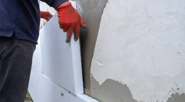Man con guantes rojos instala paneles de poliestireno para aislamiento exterior fachadas.
