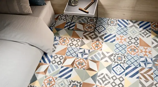 Un suelo con **baldosa hidráulica** de diseño geométrico y colores vibrantes, junto a una cama y una mesita de noche.
