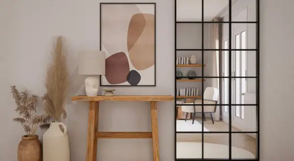 Entradas pequeñas con encanto: consola de madera, lámpara, cuadro abstracto y espejo industrial que refleja un sillón.