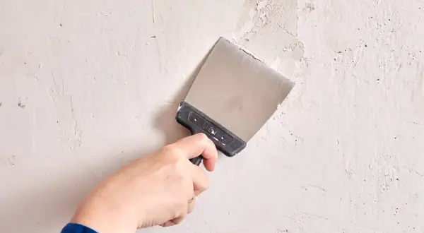 Mano con espátula aplica masilla a una pared irregular.
