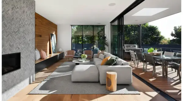 Elegante diseño de salas con chimenea de piedra, sofá modular gris, sillas rosadas y acceso a terraza con comedor exterior.
