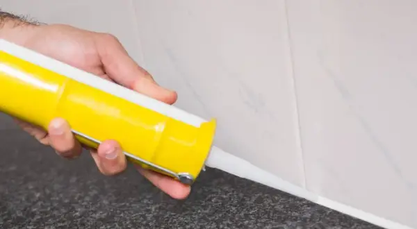 Mano aplicando silicona en juntas con pistola.