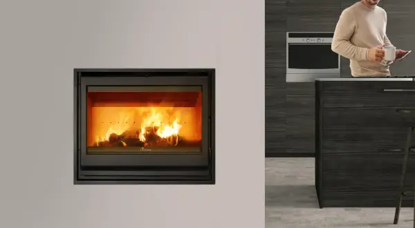Chimenea cassette con fuego encendido. Un hombre sonríe con una taza y una tablet en una cocina moderna.