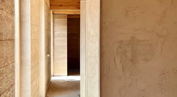 Pasillo con paredes de mortero de cal interiores, textura natural y vigas de madera en el techo.