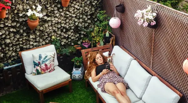 Mujer relajada en un sofá en un patio con césped artificial, luces y plantas. Ideas para decorar patio sin dinero.