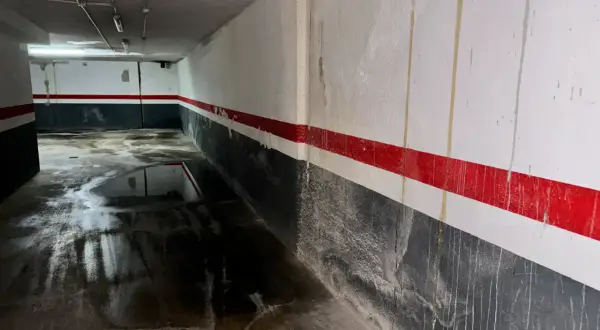 Pasillo de garaje con charcos en el suelo y marcas de humedad por filtración en las paredes pintadas con franjas rojas y grises.