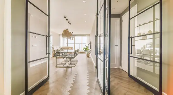 Amplio salón comedor rectangular de 25 metros, con suelo de espiga y separadores de cristal.