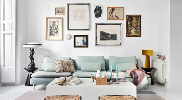 Un sofá azul claro con cojines decorativos y una colección de arte ecléctica en la pared. Ideas de qué poner detrás del sofá: una galería de arte o una estantería.