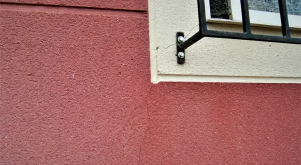 Detalle de juntas de dilatación en fachadas de color rojo y crema, con una ventana enrejada.
