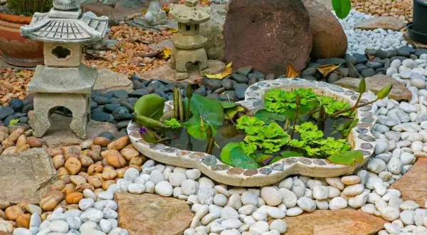 Un sereno jardín zen japonés con un estanque de lotos, linternas de piedra y rocas de diferentes tamaños.