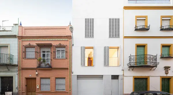 Fachada edificio con ladrillo visto y detalles de azulejos, junto a una moderna construcción blanca y otra amarilla con balcones de forja.