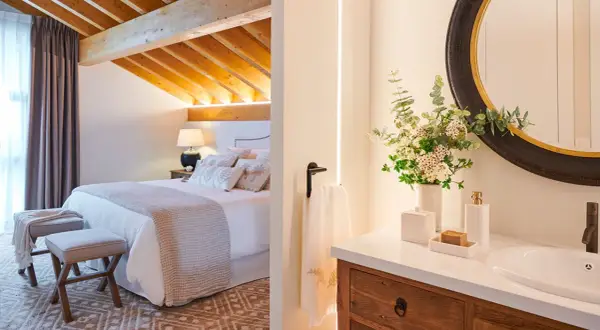 Habitación con vigas de madera y baño con espejo redondo. ¿Cuanto mide una habitación normal? Esta parece espaciosa.