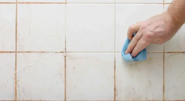 Mano limpiando juntas de azulejos sucias con un paño azul.