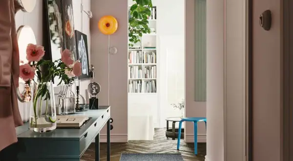 Un recibidor con pasillos con encanto: un escritorio azul, flores rosas, libros y un taburete.