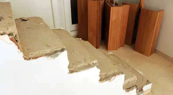 Preparativos para revestir escalera antigua. Tablas de madera apiladas junto a escalones de hormigón en proceso de reforma.